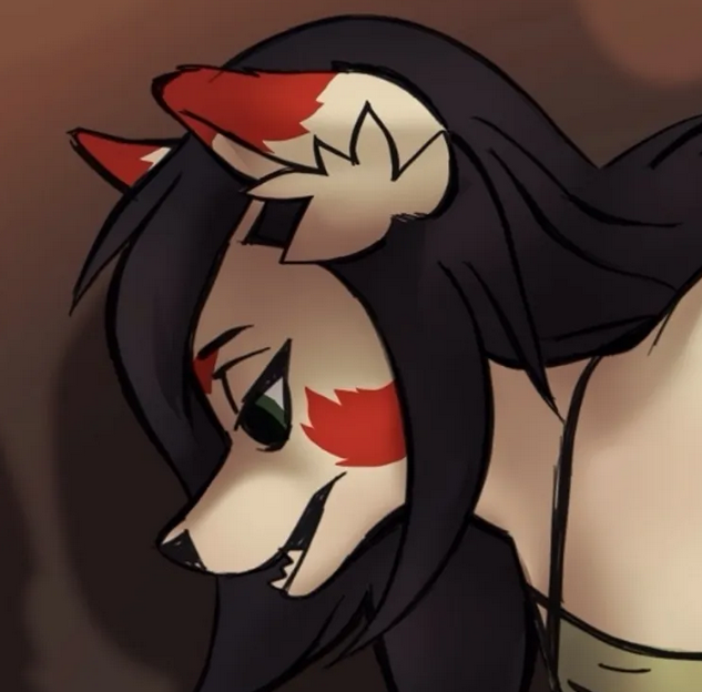 A white fox with red markings on her cheeks and ear tips with black hair. She is looking down at something off frame.